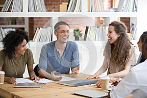 Smiling multiracial millennial colleagues laugh talking at meeting