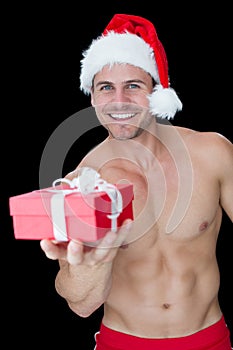 Smiling muscular man posing in santa outfit offering gift