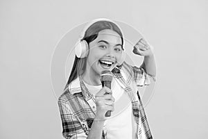 smiling music singer girl in headphones. young girl singing into music microphone isolated on yellow. teenage singer