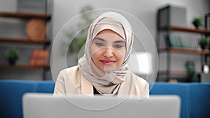 Smiling Muslim female business freelancer working laptop browsing internet at home couch closeup