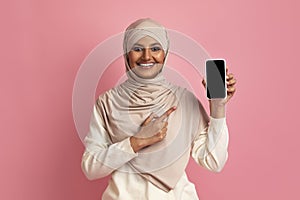 Smiling Muslim Lady Pointing At Blank Smartphone With Black Screen In Hand