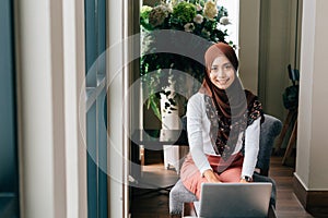 Smiling Muslim woman using laptop in cafe