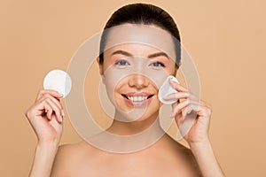Smiling naked asian girl removing makeup from face with cotton pads