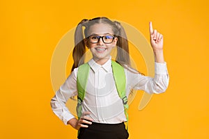 Smiling nerdy schoolgirl pointing finger up having idea, yellow background