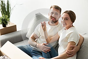 Smiling new homeowners couple holding house keys looking at came