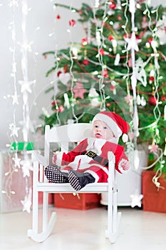 Smiling newborn baby boy in Santa costume under Christmas tree