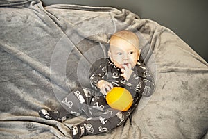 Smiling newborn baby with orange fruit sitting on sofa or couch