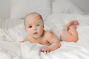 Smiling newborn baby on a white bed at home, the concept of a happy healthy infant baby. Generation alpha and gen alpha