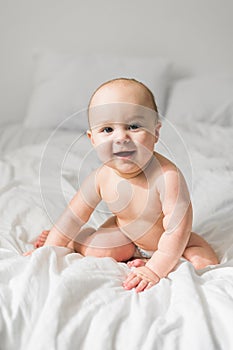 Smiling newborn baby on a white bed at home, the concept of a happy healthy infant baby. Generation alpha and gen alpha