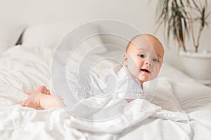 Smiling newborn baby on a white bed at home, the concept of a happy healthy infant baby. Generation alpha and gen alpha