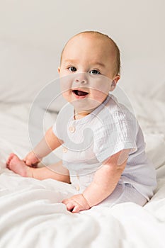 Smiling newborn baby on a white bed at home, the concept of a happy healthy infant baby. Generation alpha and gen alpha