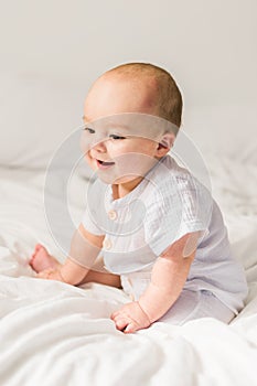 Smiling newborn baby on a white bed at home, the concept of a happy healthy infant baby. Generation alpha and gen alpha