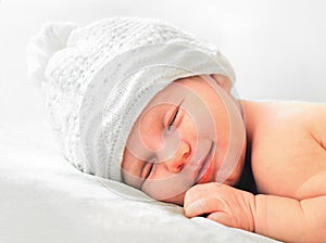Smiling newborn baby in white hat close up