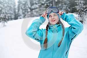 Smiling nordic woman with pigtails puts on protective ski goggles. Snowboarder girl touching mask at ski resort on