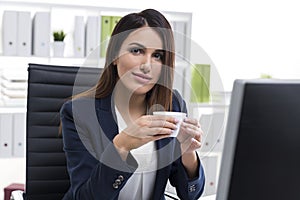 Smiling and nostalgic businesswoman with a cup of coffee in an o