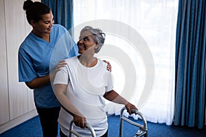 Smiling nurse assisting senior woman in walking with walker