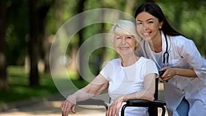 Smiling nurse and handicapped woman in wheelchair smiling camera, caring staff