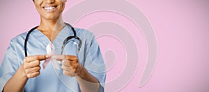 Smiling nurse holding breast cancer awareness pink ribbon with both hands