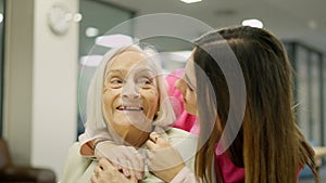 Smiling nurse kissing and embracing a senior woman in geriatrics
