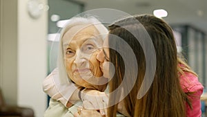 Smiling nurse kissing and embracing a senior woman in geriatrics