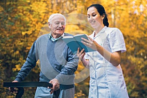 Smiling nurse reading book to senior man that uses walker