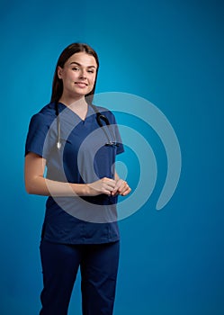 Smiling nurse with stethoscope standing, looking ahead, blue background