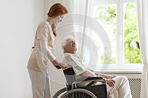 Smiling nurse supporting disabled senior man in the wheelchair