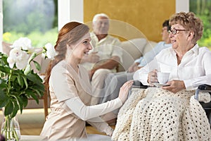 Smiling nurse taking care of disabled senior woman in the nursing house
