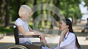 Smiling nurse talking with disabled elderly woman in park, rehabilitation center