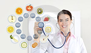 Smiling nutritionist doctor with stethoscope pointing symbols fruits icons and medical texts isolated on white background, healthy