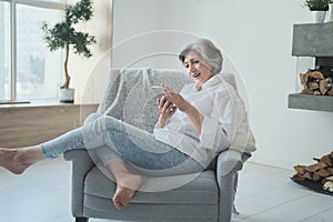 Smiling old adult lady enjoying using smartphone application reading positive news,