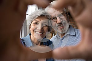 Smiling old age couple unite fingers before camera in heart