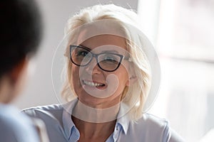 Smiling old businesswoman looking at colleague listening client at meeting