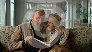 Smiling old couple looking photo album room. Mature man woman talking home.