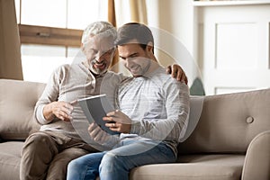 Smiling old dad and adult son use tablet at home