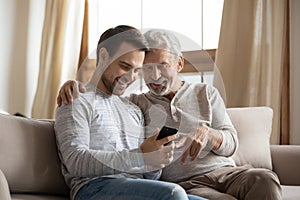 Smiling old dad and grownup son use cellphone