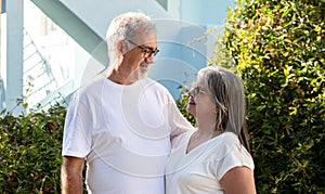 Smiling old european husband and wife in white t-shirts hugging, enjoy spare time, outdoors
