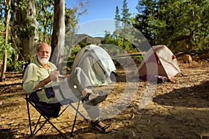 Smiling old hiker in the camp in morning forest