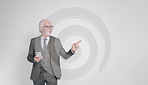 Smiling old male professional using smart phone and pointing at copy space over white background