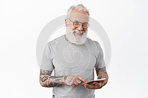 Smiling old man in glasses with tattoos, holding digital tablet, online shopping or networking, looking happy at camera