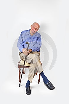 Smiling old man holding a walking stick sits on a chair