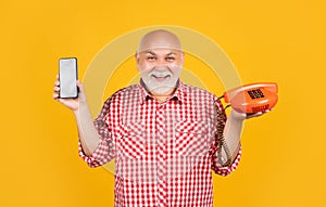 smiling old man with retro telephone and modern smartphone on yellow background