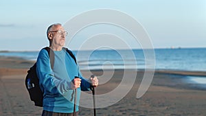 Smiling old man with Scandinavian walking stick dreaming admiring sunset sunrise sand sea beach