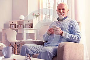 Smiling old man spending time with smartphone