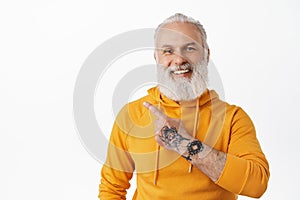 Smiling old man with tattoos pointing at upper left corner. Cool granfather with long beard wearing orange hoodie