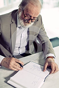 Smiling old man is writing his memories from his happy youth on the notebook