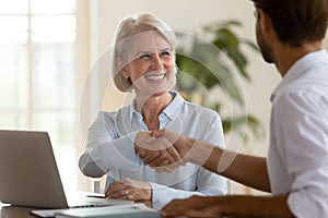 Smiling mature saleswoman handshake businessman client customer at business meeting