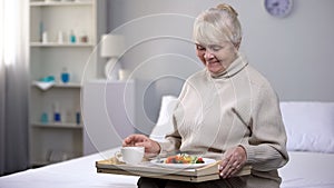 Smiling old woman eating dinner in nursing home, social security for aged people