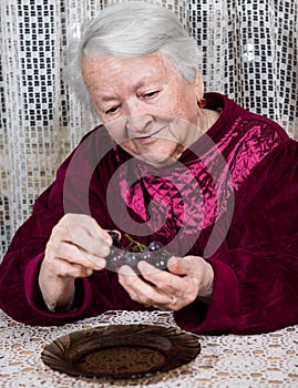 Smiling old woman eating grapes