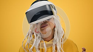 Smiling old woman watching film in vr glasses on yellow studio background.